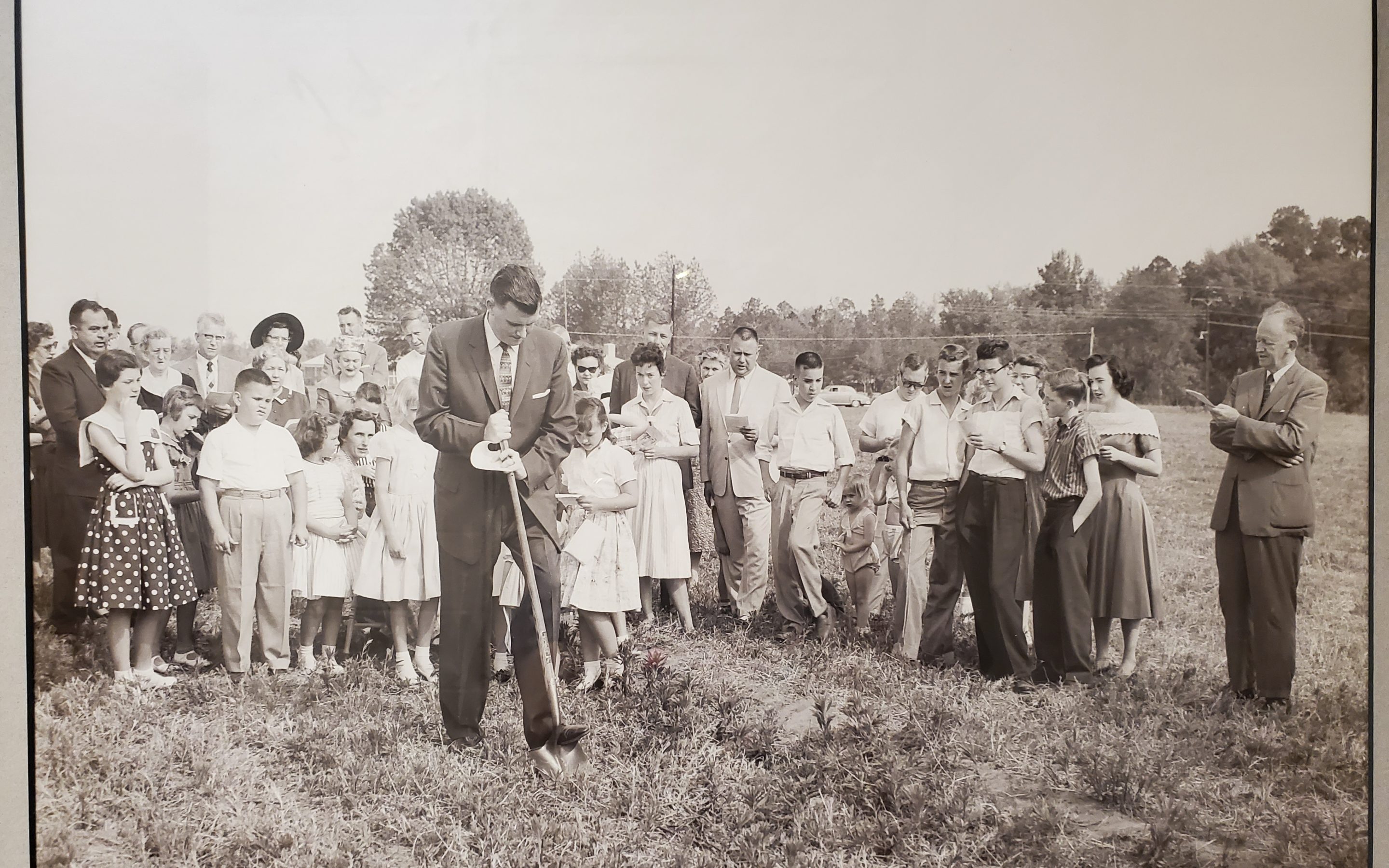 A group of people looks on as a man holds a shovel in a field