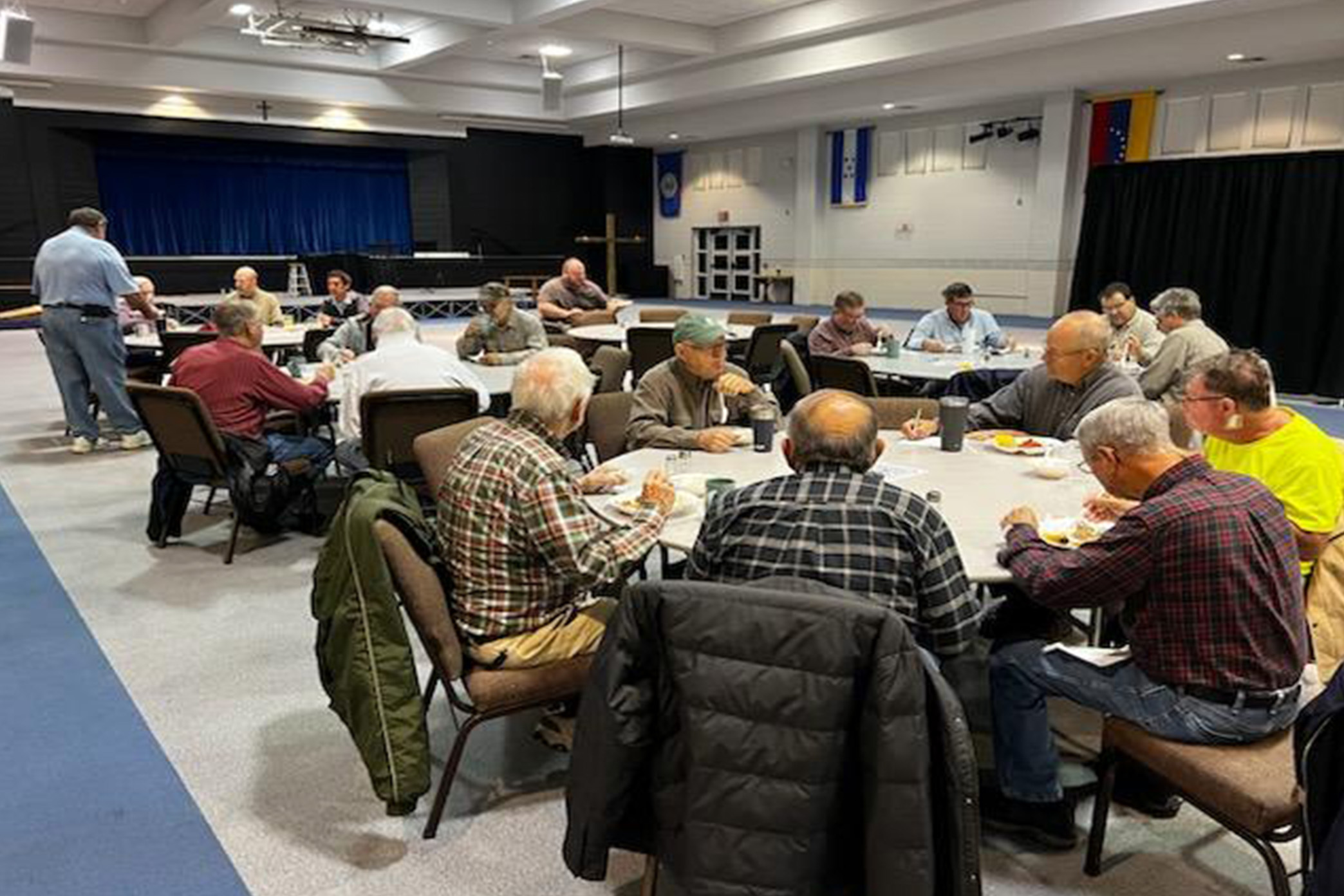 Photo of people eating around tables in the Fellowship Hall