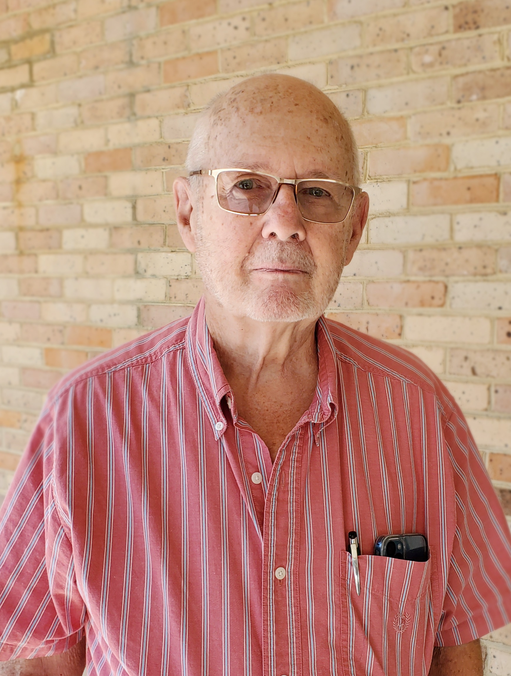 Portrait of elderly man in glasses and collard shirt with a phone and pen in his pocket