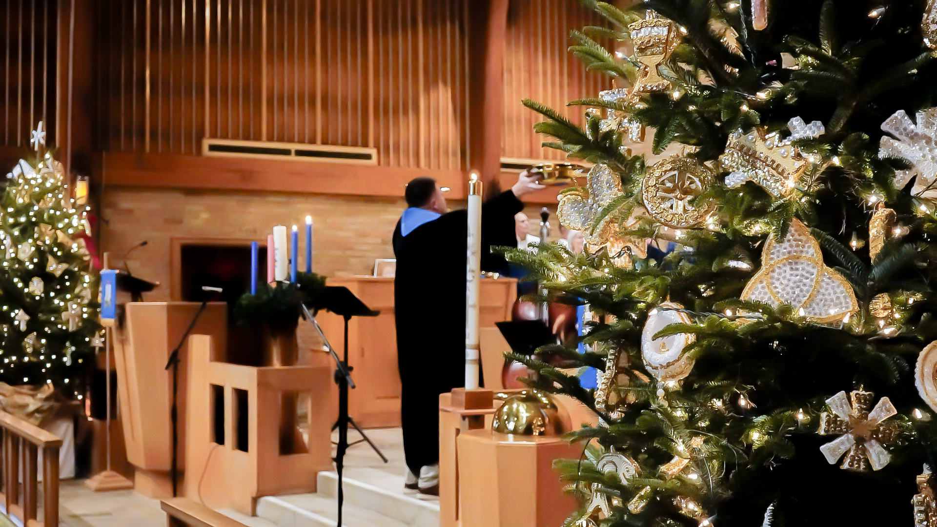 Photo of the front of the sanctuary from the angle of the right Christmas tree with Advent candles, Christ candle and Pastor in the scene