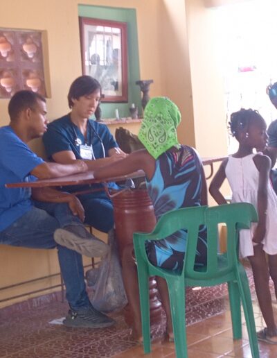 Man in scrubs and man in a t-shirt sit across the table from a woman with a head scarf and two small children