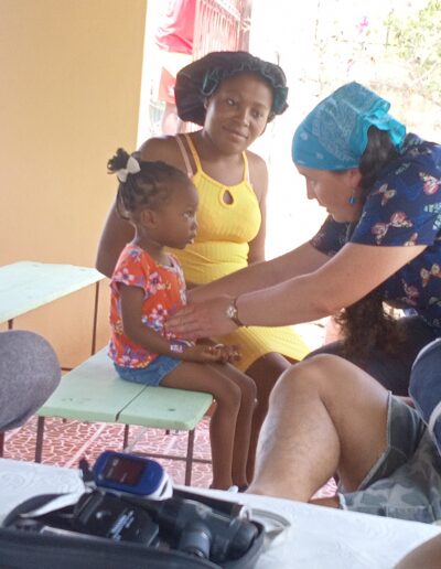 Woman in scrubs touches the belly of a toddler while a soman in a tank top watches